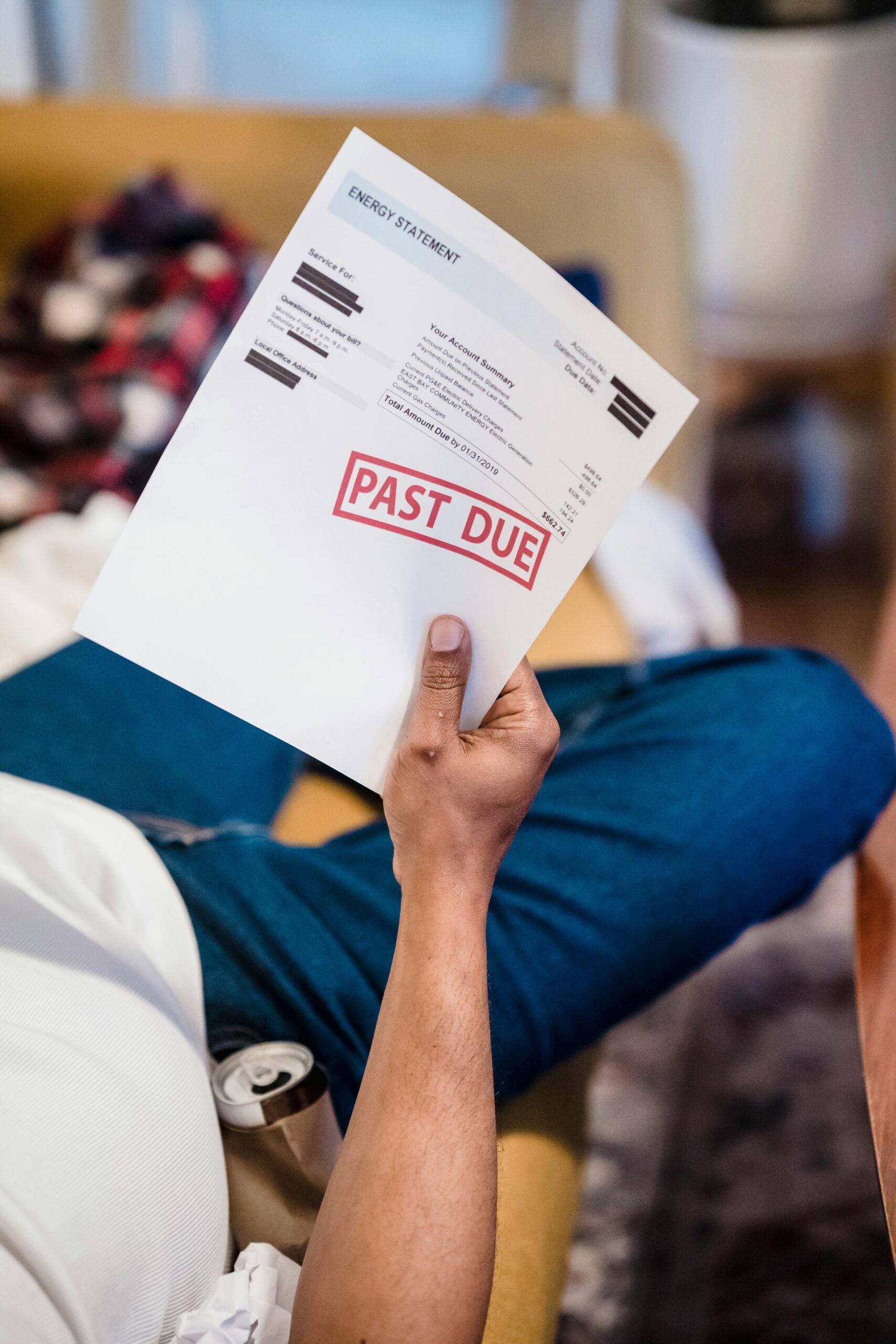 A man holding a past due billing statement while lounging indoors, expressing financial stress.