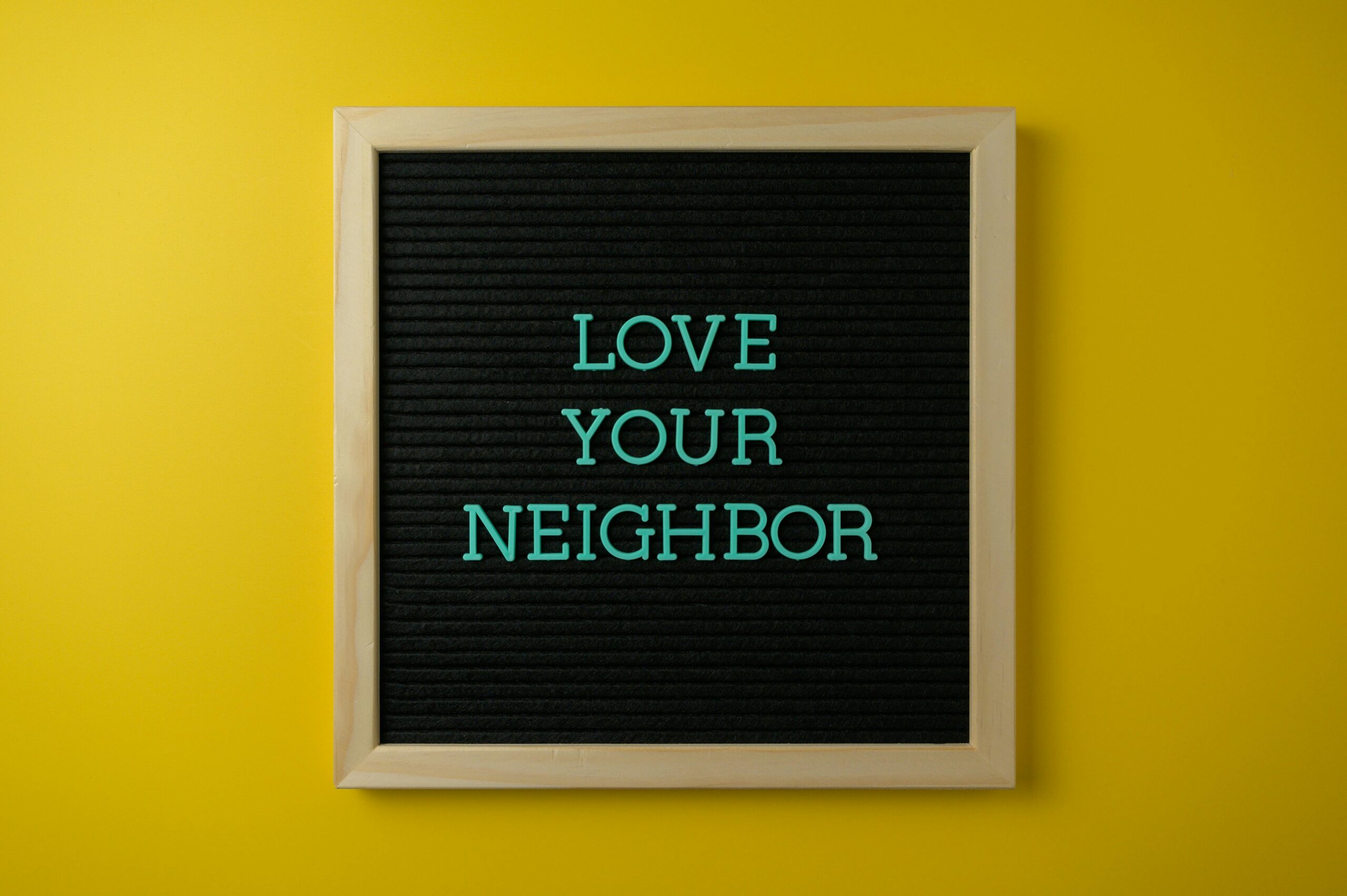 A motivational message "Love Your Neighbor" on blackboard against a yellow wall.